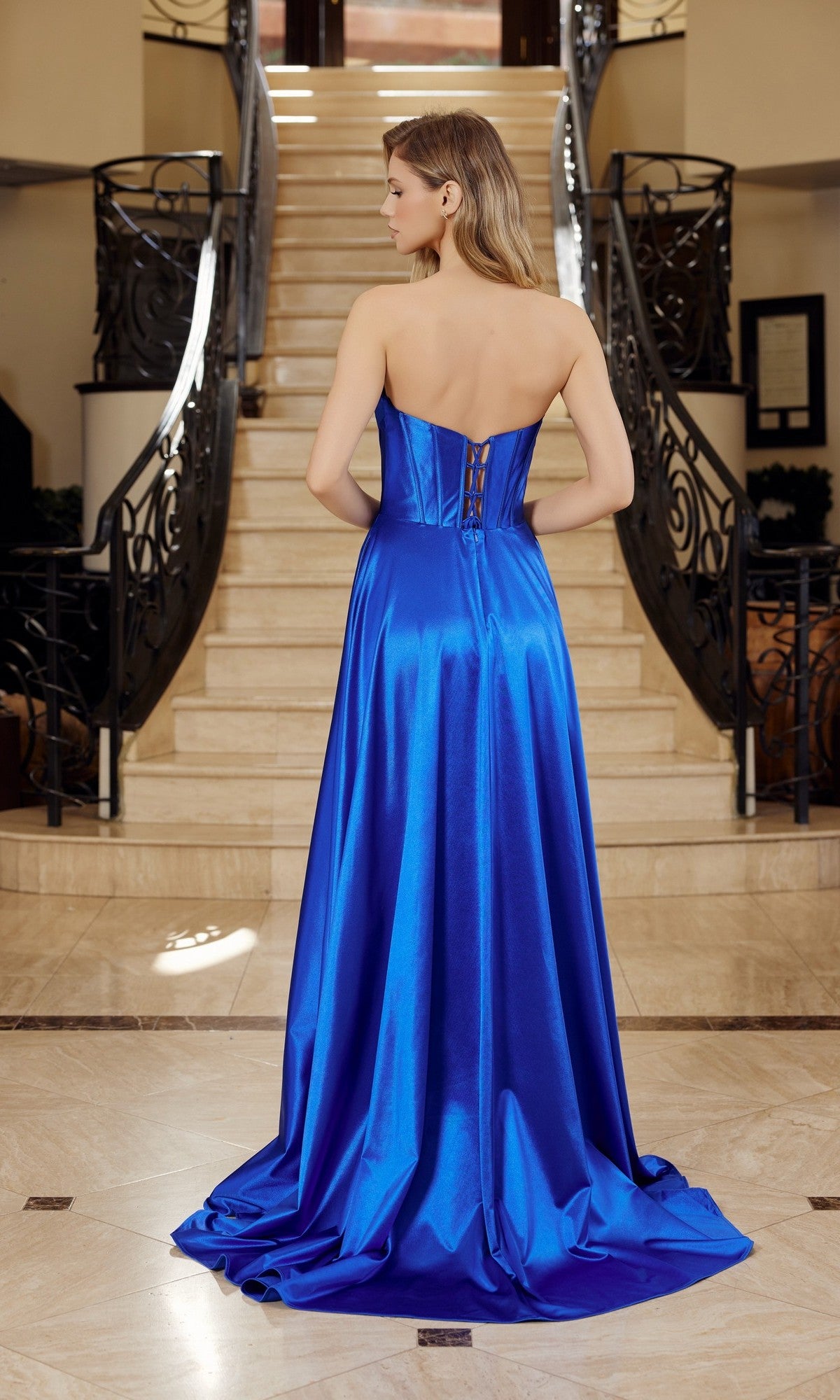 A woman in the Nox Anabel K1735 Long Prom Dress, featuring a strapless satin bodice and elegant A-line skirt, stands at the base of a staircase with her back to the camera.